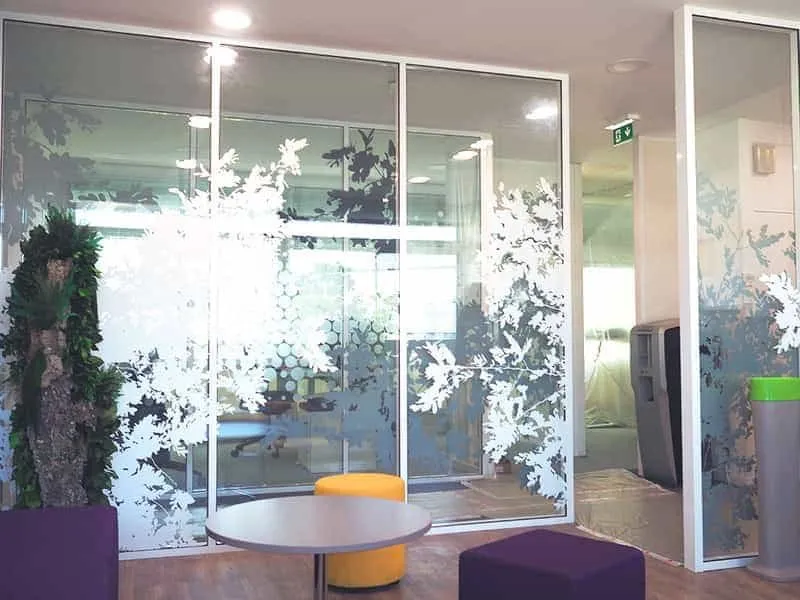 Espace de détente de bureaux derrière des cloisons vitrées habillées d'arbres blancs