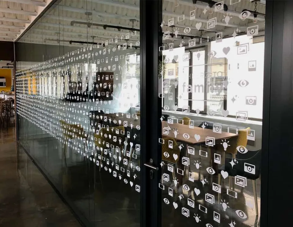 Cloison vitrée à cadre noir habillée de pictogrammes blancs