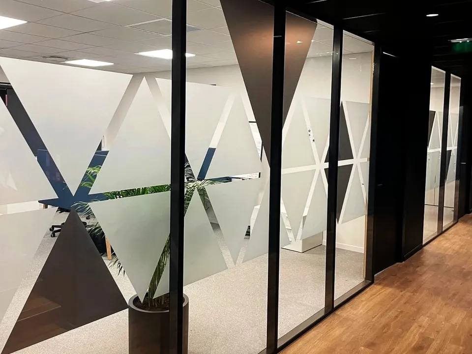 Couloir de bureaux avec cloisons vitrées habillées de grands triangles noirs et de bandes dépolies