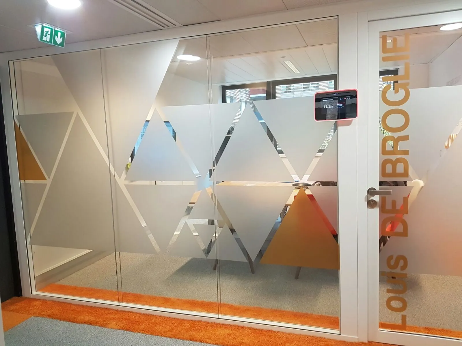 Salle de réunion vitrée avec triangles de couleur et nom de salle en lettres adhésives